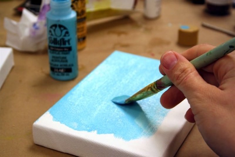 Painting a canvas with blue acrylic paint