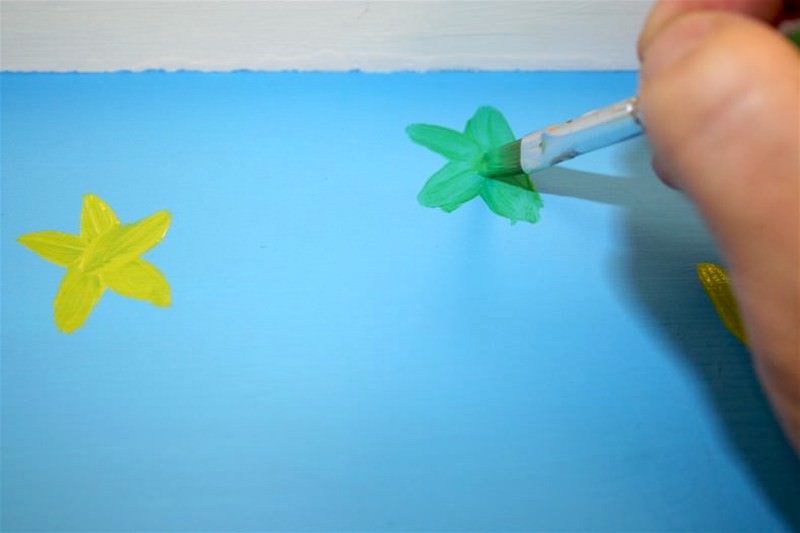 Painting flowers on the side of a table with craft paint