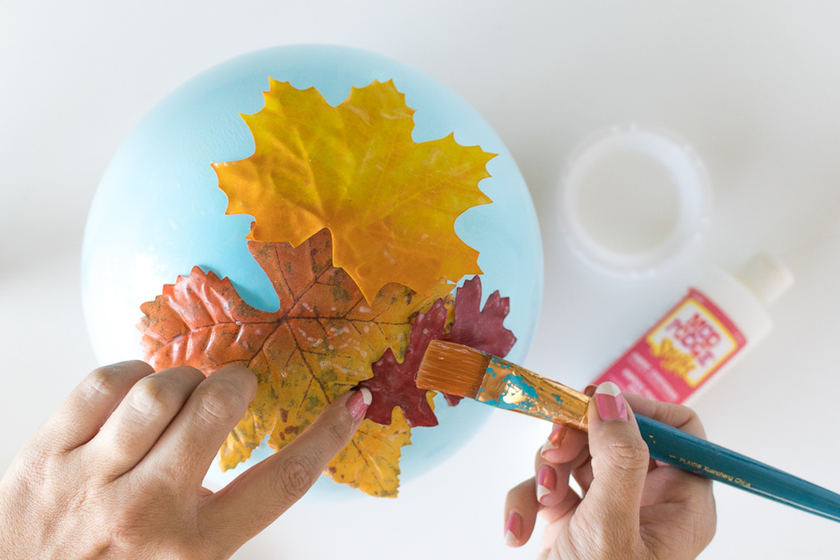 Applying leaves to a balloon with Mod Podge Stiffy and a paintbrush