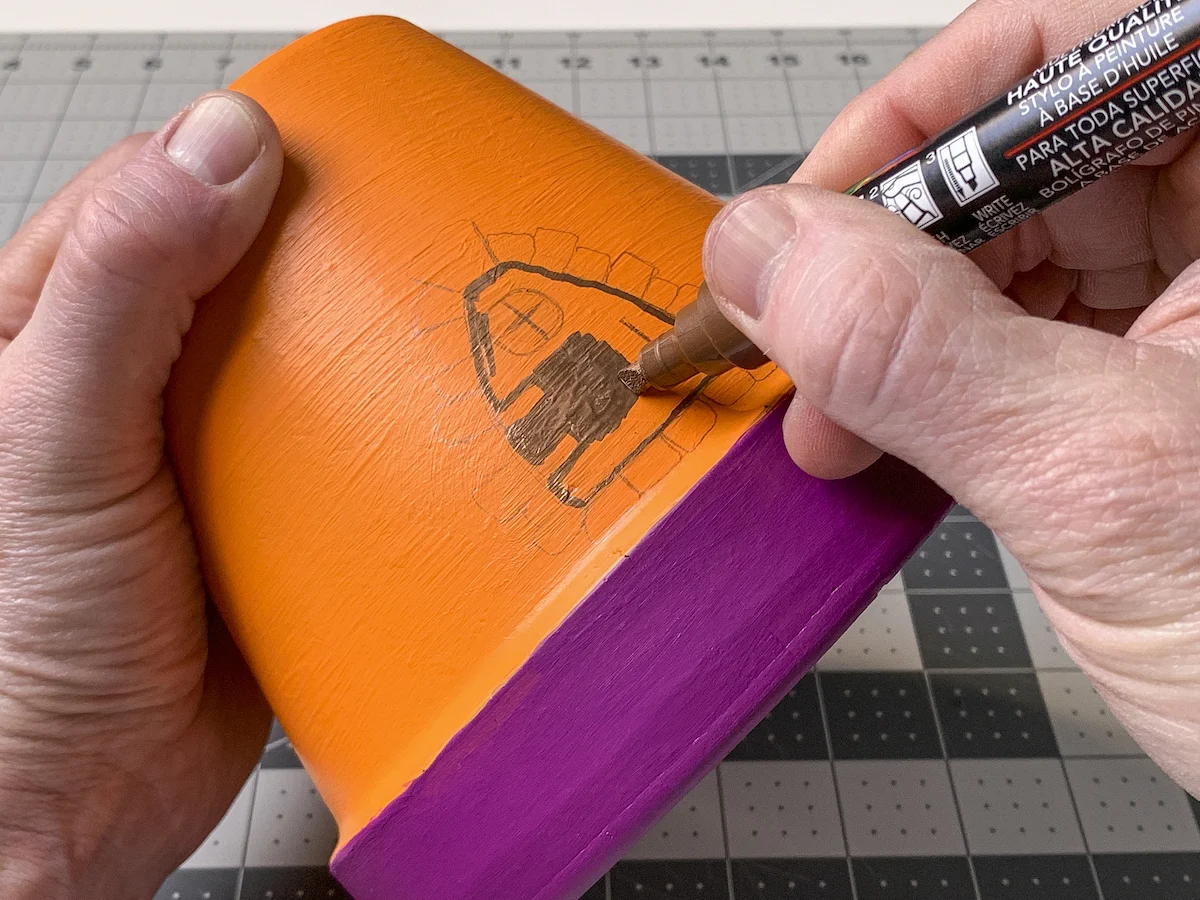 Drawing a fairy door on a clay pot with a paint pen
