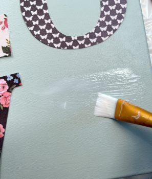 Applying Mod Podge to the canvas to apply a letter E