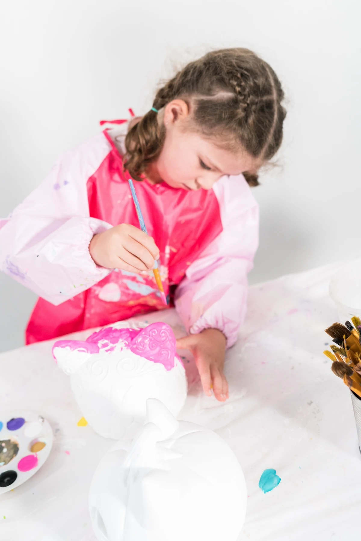 Child-wearing-a-smock-painting-a-surface-with-pink-paint
