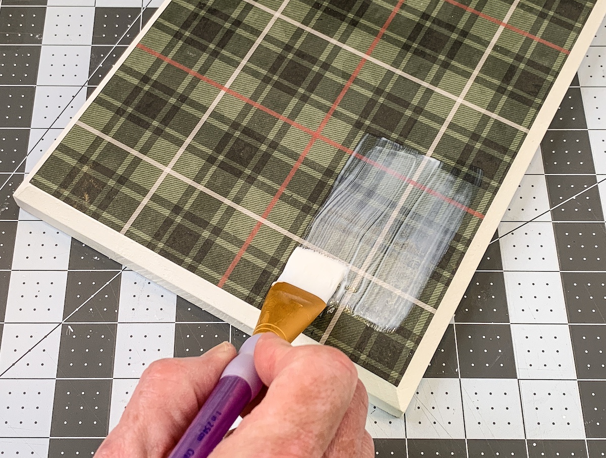 Painting Mod Podge on top of plaid paper with a paintbrush