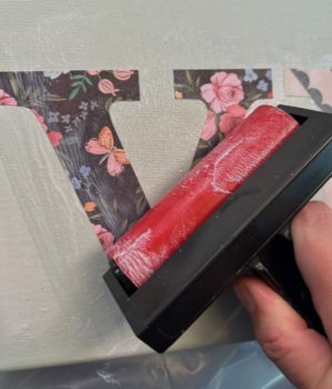 Smoothing down the letter V on canvas with a brayer