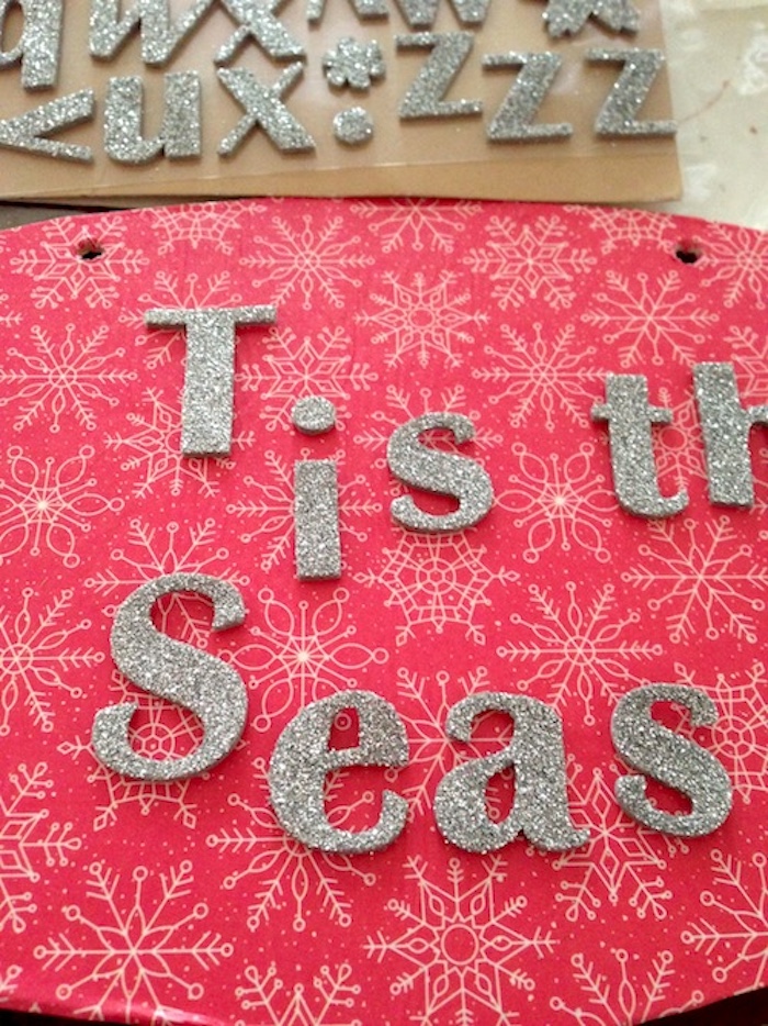 applying adhesive letters that say tis the season to the wood ornament