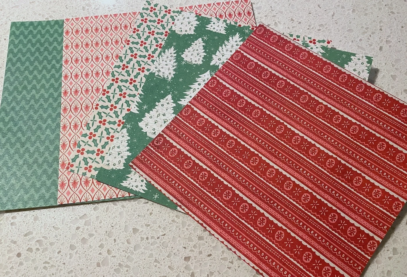 Five sheets of Christmas scrapbook paper spread out on a counter