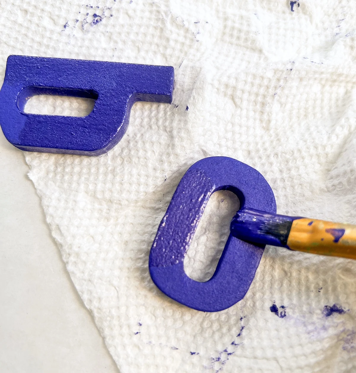 Painting wood letters spelling boo with purple paint