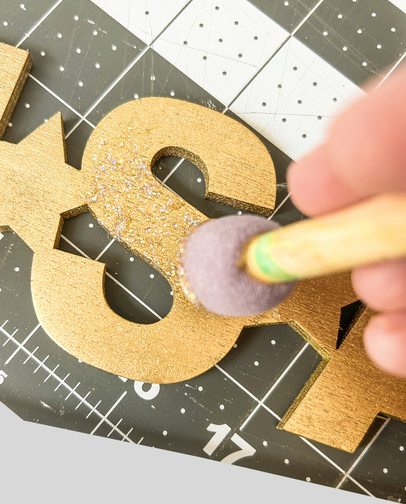 Using a spouncer to apply glitter paint to the gold word