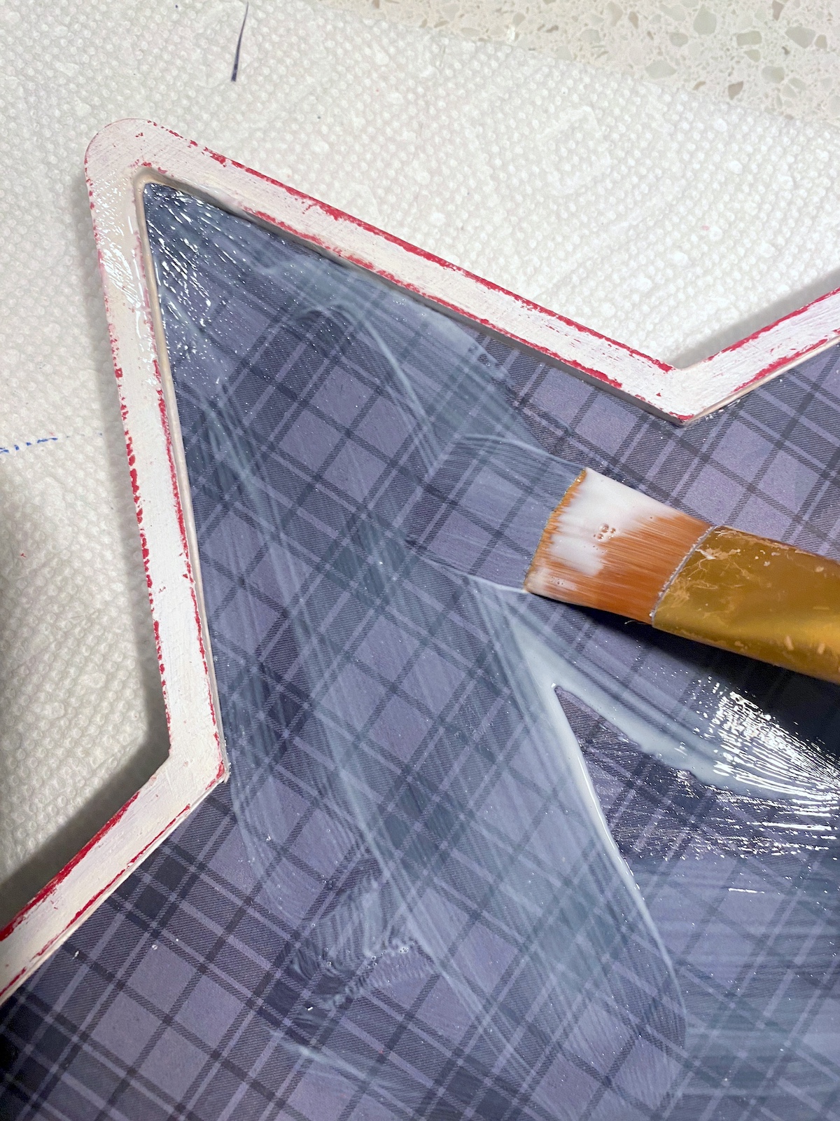 Applying Mod Podge to the top of the plaid paper