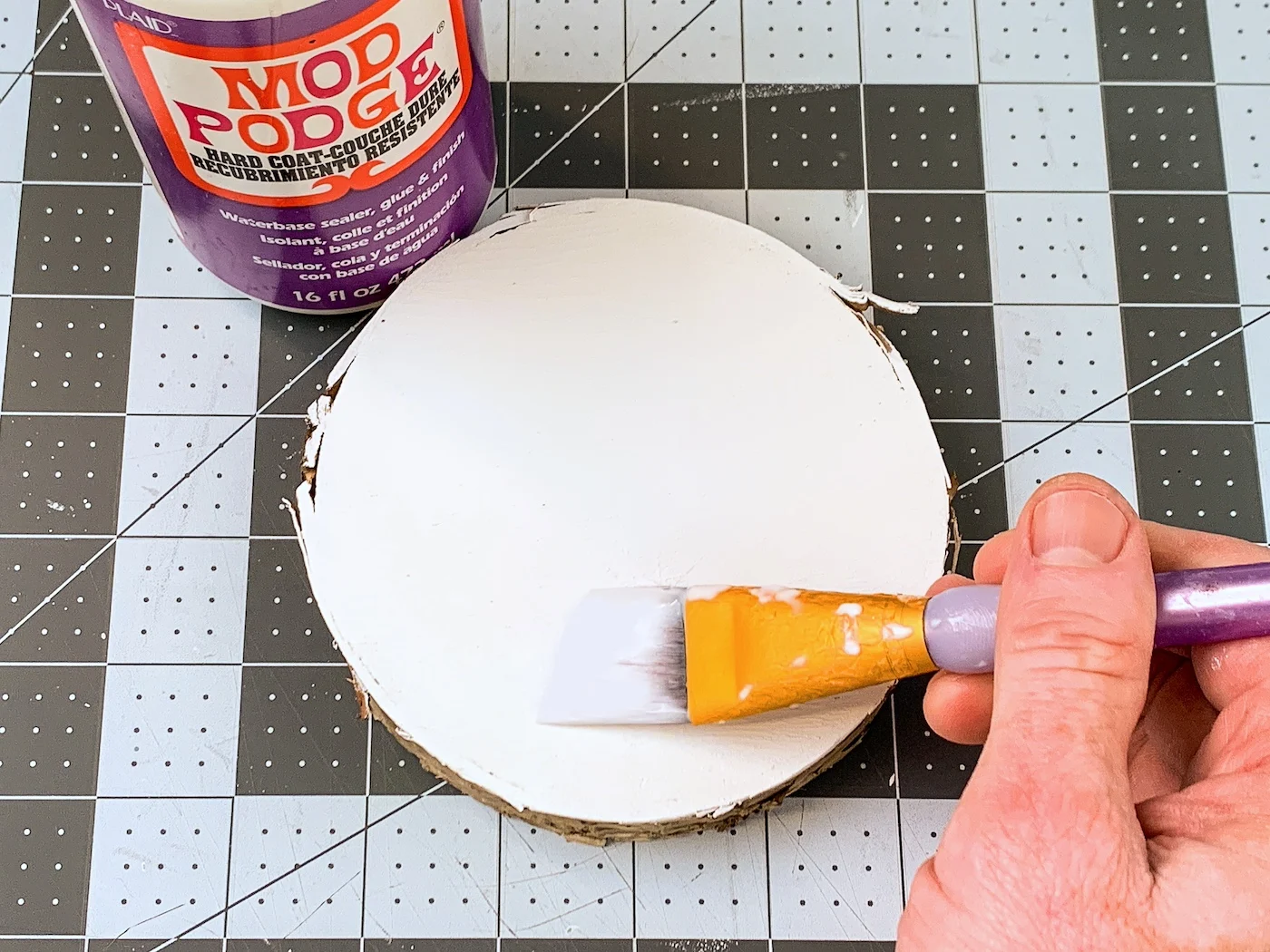 Applying a layer of Mod Podge to a wood slice