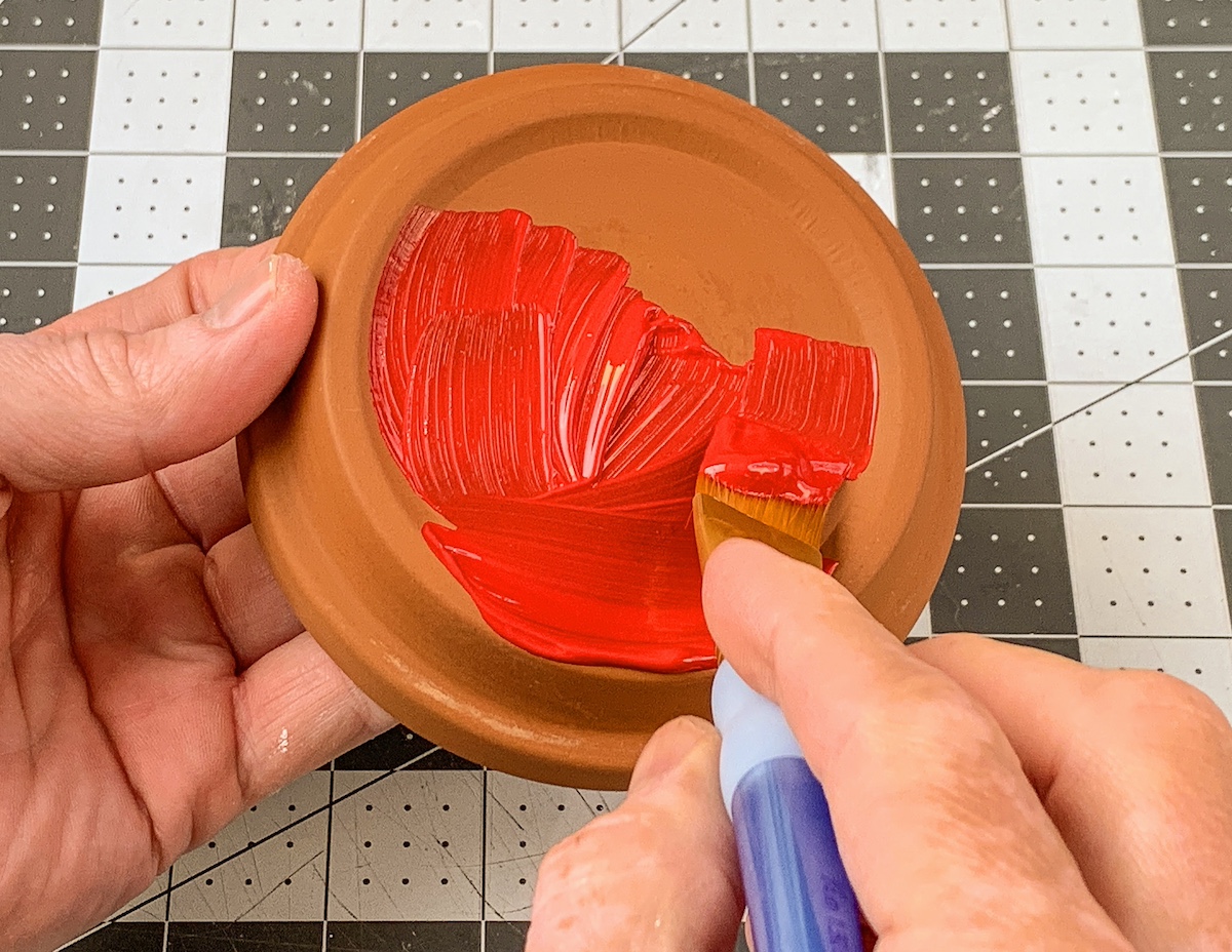 Painting a clay pot saucer with red paint