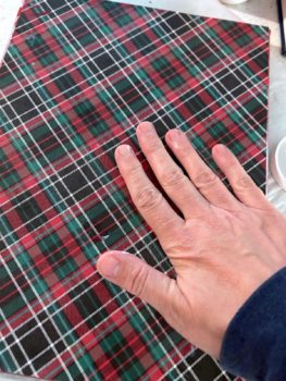 smoothing plaid paper down onto the canvas